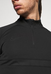 Schwarzes Sportoberteil mit hohem Kragen, Viertel-Reißverschluss, strukturiertem Einsatz über der Brust und dezentem Nike-Logo.