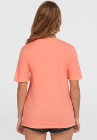 Camiseta de algodón coral de manga corta con un escote redondo y un corte holgado, que presenta una pequeña etiqueta en el dobladillo.
