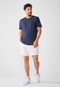 Cămașă scurtă cu maneci, texturată, de culoare bleumarin, cu un buzunar pe piept, asortată cu pantaloni scurți din in alba și adidași albi. O ținută simplă și lejeră.