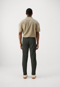 Camicia a maniche corte di un leggero colore beige, con colletto, abbinata a pantaloni verde scuro dal taglio dritto e con tasche posteriori. Design semplice e pulito.