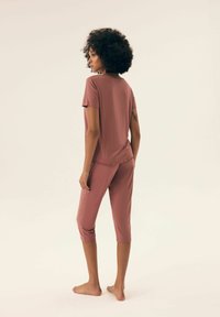 Dwuczęściowy zestaw odzieży do wypoczynku wykonany z miękkiego, różowego materiału. Krótki top z zaokrąglonym dołem oraz spodenki 3/4 z dopasowanym pasem.