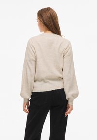 Beige knitted sweater with a round neckline, long balloon sleeves, and a soft texture, worn over black pants. Casual fit and slightly cropped.