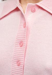 Ροζ ζακέτα από απαλό πλεκτό με υφασμένη γιακά, διαθέτει έξι κουμπιά στο ίδιο χρώμα κατά μήκος του μπροστινού μέρους και ριμπ λεπτομέρειες στα άκρα.