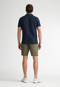 Polo bleu marine à finition texturée, short kaki et chaussures de sport blanches, vus de dos, mettant l'accent sur des lignes épurées et une coupe ajustée.