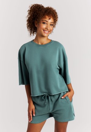 Oversized sweatshirt in blauwgroen met korte mouwen en een onafgewerkte zoom, gecombineerd met bijpassende shorts met een trekkoord en zijzakken.