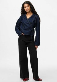 Tumša džinsa iesaiņošanas topiņš ar garām piedurknēm, V veida izgriezumu un tonētiem diegiem. Kopā ar melnām platajam bikšu kājām un sarkaniem apaviem.