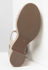Sandal con tacco alto beige, suola in gomma testurizzata, sottile cinturino per la caviglia e design minimalista. Marchio visibile sulla suola.