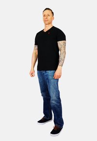 Black V-neck t-shirt with a red logo, paired with blue denim jeans and black sneakers with brown laces, against a plain background.