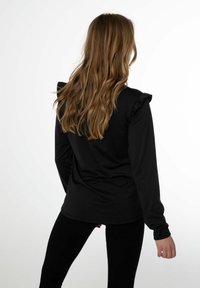 Zwarte lange mouw top met ruffle accenten op de schouders, gemaakt van een gladde stof, gedragen met zwarte leggings.