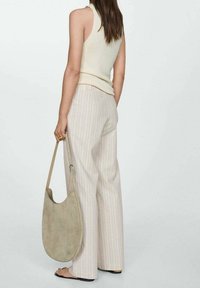 Vrouw in een crème mouwloos top en beige gestreepte wijde broek met een grote beige suède schoudertas en zwarte sandalen.