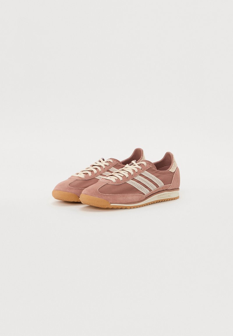 Baskets en suede rose avec des accents de rayures blanches, des lacets crème et une semelle en caoutchouc texturée. Présente un design bas.