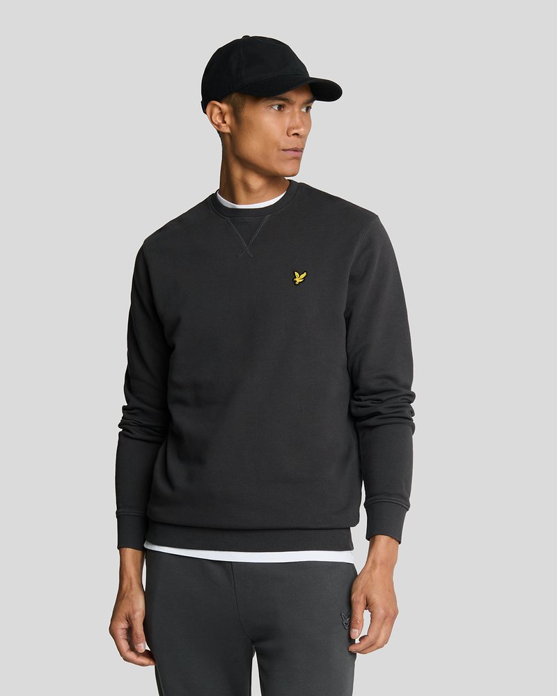 Black sweatshirt made of cotton blend, features ribbed cuffs and hem, with a small yellow logo on the chest. Worn with a black cap.