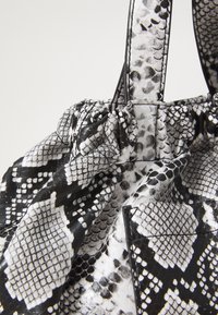 Borsa nera e bianca in finta pelle di serpente con parte superiore arricciata, texture liscia e tasca laterale rettangolare con un design a fantasia.
