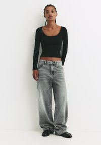 Schwarzes, tailliertes Langarmshirt kombiniert mit hoch taillierten, weiten grauen Jeans, die mit einer verwaschenen Optik und minimalistischen Steppnähten versehen sind.