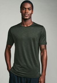 Dark green short-sleeve shirt with a textured pattern and round neckline. Soft fabric drapes close to the body. Features a small logo on the hem.