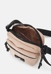 Borsa compatta in tessuto beige con superficie texturizzata, zip nera e cinturino regolabile. L'interno è foderato con un materiale liscio.