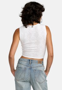 White crocheted tank top with a fitted design, featuring a textured pattern. Paired with high-waisted blue distressed denim jeans.