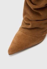 Bottine en daim marron avec un bout pointu et un matériau froncé, mettant en valeur une texture lisse et des détails de design minimalistes.