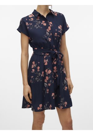 Donna che indossa un vestito blu navy a maniche corte con stampe floreali rosa, un colletto e una cintura annodata in vita.