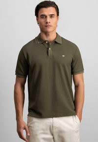 Olijfgroene polo shirt met korte mouwen, twee-knopen kraag en contrasterende stiksels. Heeft een subtiele logo op de borst.