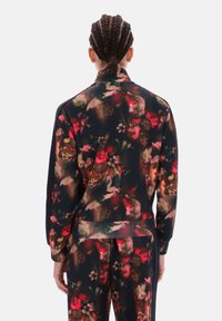 Čierna priehľadná vrchná časť teplákovej súpravy s kvetinovým vzorom, dlhými rukávmi a voľným strihom, zdobená žiarivými červenými a zelenými abstraktnými kvetmi.