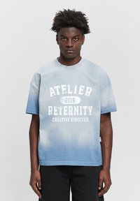 Light blue cotton t-shirt with an ombre effect, featuring white printed text: "ATELIER RETERNITY 2018 CREATIVE DIRECTOR." Short sleeves.