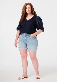 Navy V-hals top met textuur van bloem borduursel op puff mouwen, gecombineerd met lichtblauwe denim shorts met omgeslagen zoom en witte sandalen.