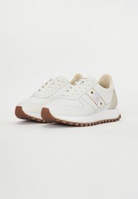 Sneaker bianche con suola in gomma testurizzata, con accenti marrone chiaro, lacci e parte superiore in pelle liscia con sottili strisce laterali.