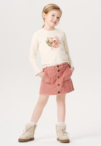 Langærmet cremetop med blomstermotiv og en pink kordfløjlsskjorte med forlommer og brune knapper. Komplementeret med beige støvler.