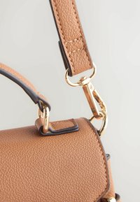 Tan pebbled leather handbag with gold hardware accents, featuring a structured shape and a contrasting dark trim on the shoulder strap.