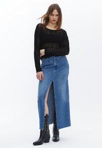 Svart, stickad tröja med lös väv, matchad med en lång blå denimkjol med en framficka och hög midja, buren med svarta stövlar.