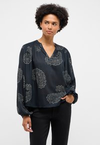 Mustast paisleimustriga pikkade varrukatega pluus, V-kaeluse, kogutud õlgade ja elastsete mansettidega, valmistatud siledast, kergest kangast.