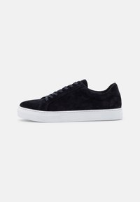 Adidași negri din suede cu talpă plată din cauciuc alb, vârf rotund și șase ochiuri pentru șireturi. Textură netedă cu detalii de cusătură subtile.