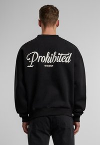 Felpa nera con vestibilità oversize, caratterizzata da testo in corsivo bianco che dice "Proibito" e "10119 BERLINO" sul retro. Materiale in cotone.