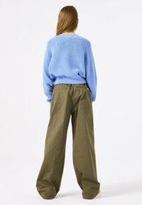 Lichtblauwe gebreide trui met ribbelstructuur, gecombineerd met losse olijfgroene broek. De broek heeft achterzakken en een wijd model.