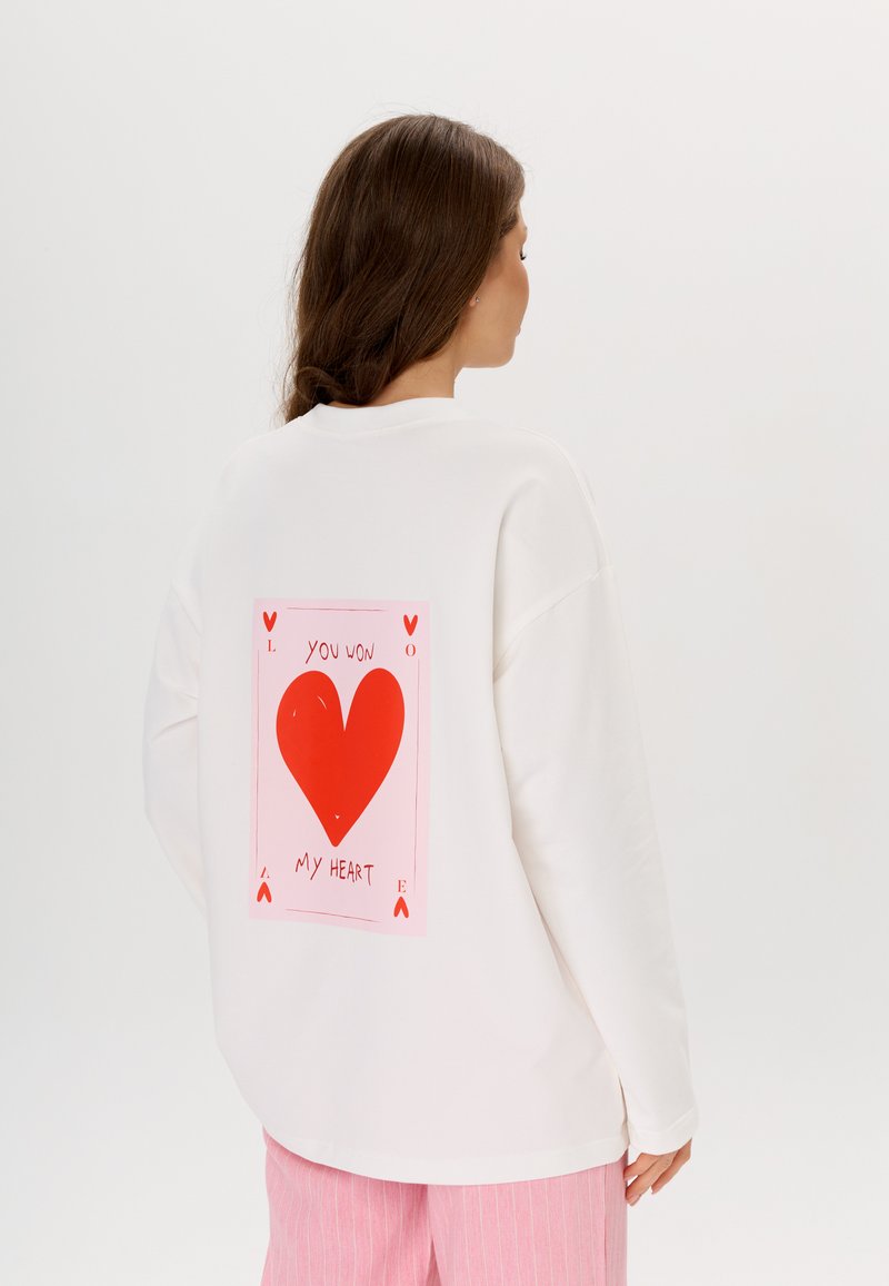 Felpa bianca oversize con una grande grafica a forma di cuore rosso e scritta "MI HAI RUBATO IL CUORE" sul retro. Tessuto morbido con una vestibilità rilassata.