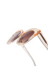 Ochelari de soare supradimensionați, cu lentile maro degradé, rame transparente de piersici și brațe subțiri din metal. Formă notabilă a lentilelor rotunde.
