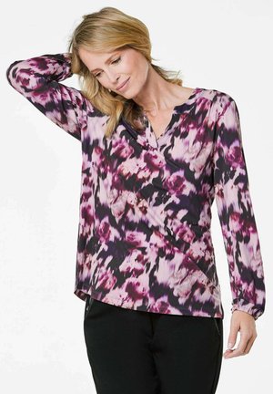 Langärmlige Bluse mit V-Ausschnitt, die ein florales Muster in verschiedenen Rosa- und Lilatönen auf dunklem Hintergrund zeigt; glatte Stoffqualität.