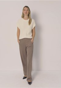 Pull crème à manches courtes associé à un pantalon large marron clair. Le mannequin porte des chaussures noires à bout pointu. Tissu lisse, coupe décontractée.