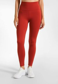 Rode legging gemaakt van soepele, rekbare stof. Heeft een hoge tailleband en past strak om het been. Gepaard met witte sportschoenen.