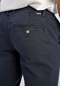 Närbild av en person som bär svarta byxor med elastisk midja och en bakficka som är säkrad med en enda knapp.