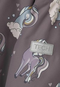 Il tessuto presenta uno sfondo viola con unicorni dei cartoni animati, nuvole, cuori e stelle; include un'etichetta grigia con la dicitura TECH. Texture liscia.