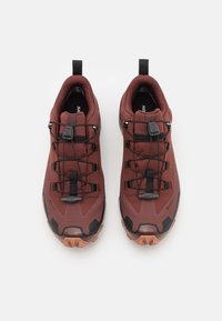 Röda och svarta sportskor med en texturerad övre del, snörningsdesign och robusta yttersulor för bra grepp. Har dragflikar för enkel påtagning.