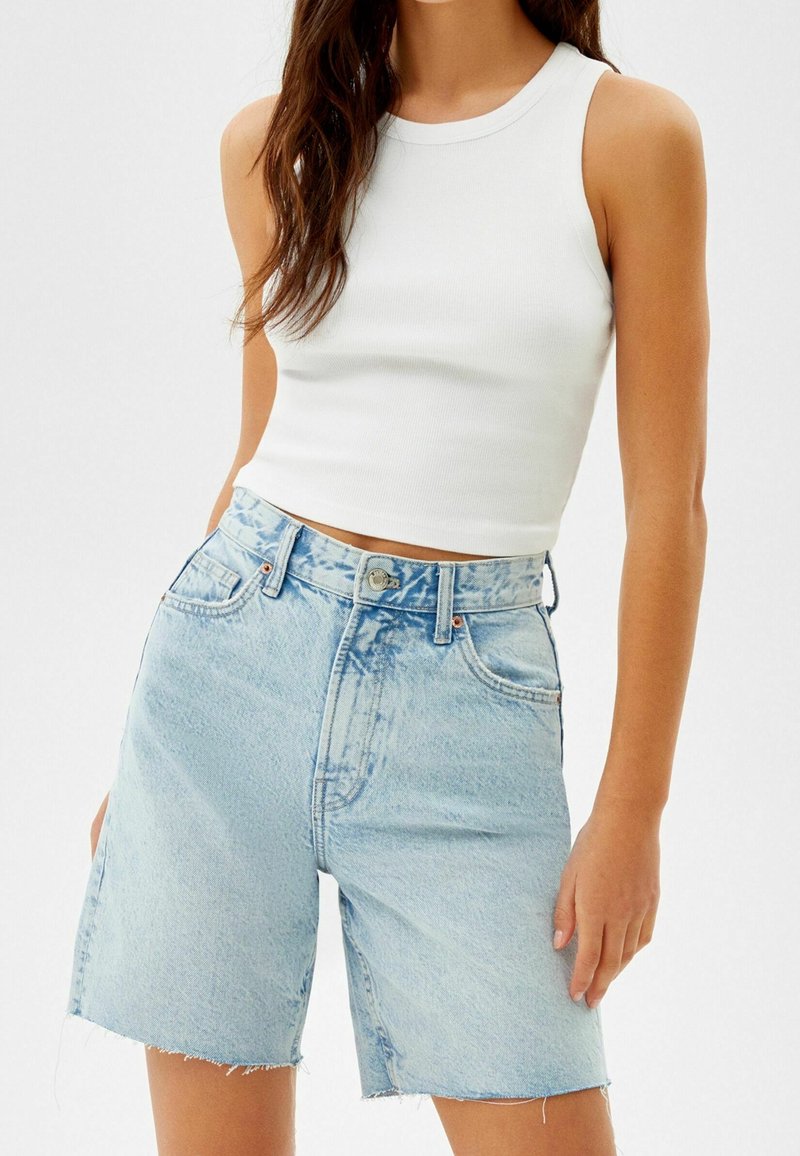 Femme portant un crop top blanc sans manches et un short en jean bleu clair taille haute avec des ourlets bruts.