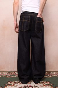 Löysät mustat farkut, joissa on keltainen ommel, kaksi takataskua, rento malli ja sileä pinta.