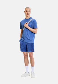 Camiseta de algodón azul con mangas cortas y un logo en el pecho; pantalones cortos de cordón azules a juego; zapatillas blancas y calcetines blancos de longitud clásica.