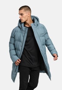 Šviesiai mėlynas pūkinis paltas su gobtuvu, su užtrauktuku ir spaudėmis, elastingomis rankovėmis ir logotipo spauda šone. Stilius su juoda marškinėliais.