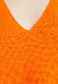 Oranges Strickoberteil mit V-Ausschnitt und strukturiertem Muster, das eine einheitliche Farbe ohne Muster oder Akzente hervorhebt.