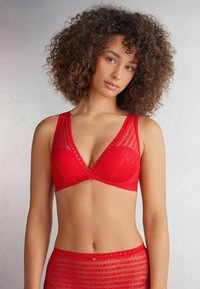 Rode kanten beha met een driehoekige vorm en doorschijnende gestreepte accenten. Heeft geschulpte randen en een klein decoratief sieraad in het midden.