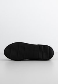 Semelle de chaussure en caoutchouc noir avec une zone centrale lisse et des rainures texturées pour l'adhérence. Forme incurvée au niveau des orteils et du talon, design globalement plat.